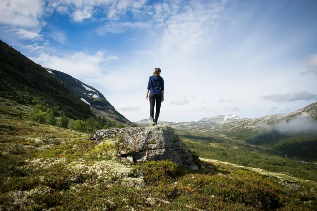 A girl stands on a rock looking out over a mountainous green valley, representing youth empowerment in environmental and resource economics.