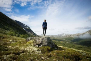 A girl stands on a rock looking out over a mountainous green valley, representing youth empowerment in environmental and resource economics.