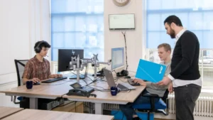 Three professionals in a modern office setting using computers and discussing documents, representing EWMagWork’s workplace management and conflict resolution practices in 2025.