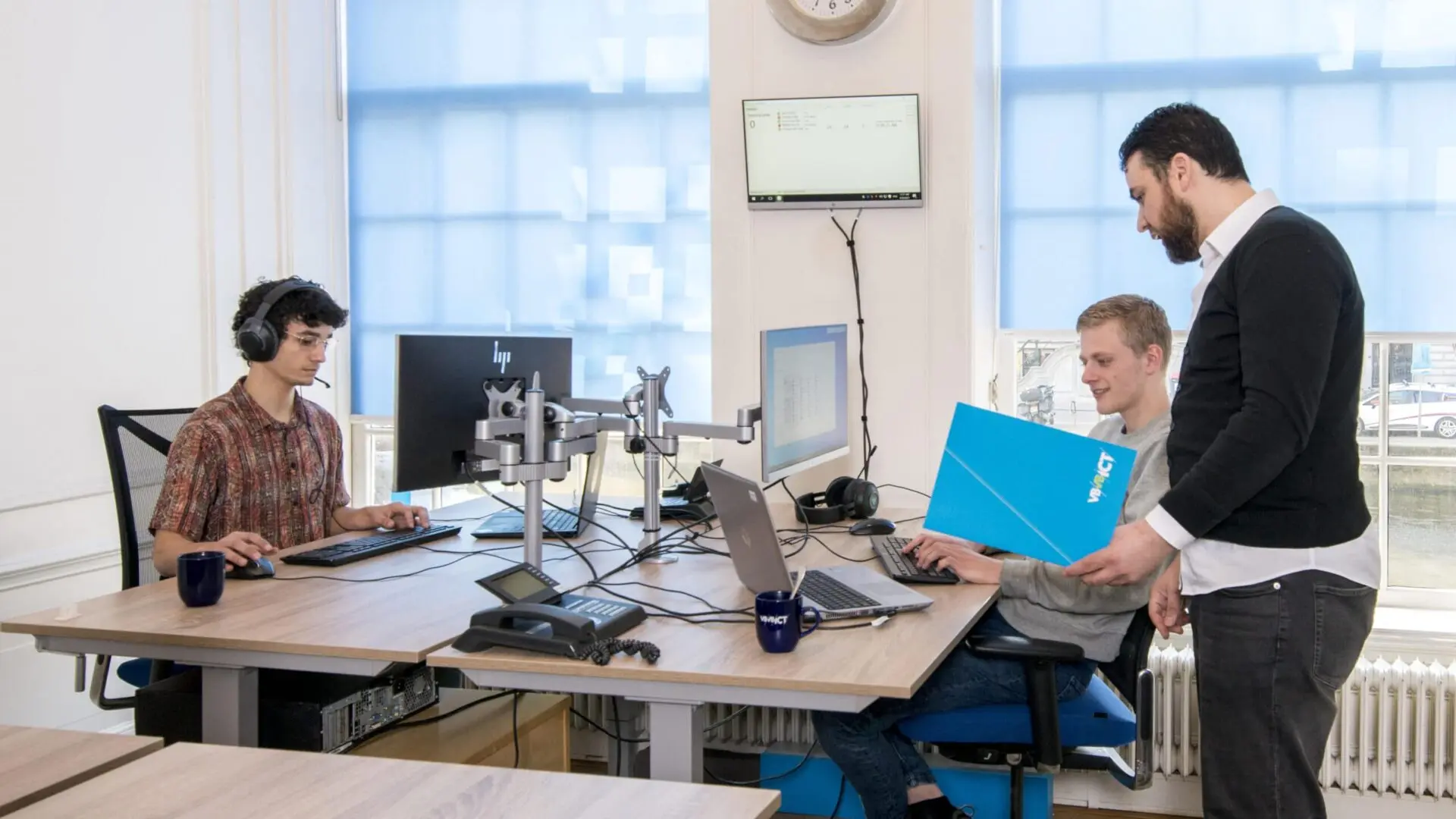 Three professionals in a modern office setting using computers and discussing documents, representing EWMagWork’s workplace management and conflict resolution practices in 2025.