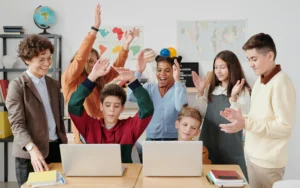 Excited students celebrating while using laptops in a modern classroom, showcasing the high energy and engagement that tools like Gimkit bring to learning in 2025.