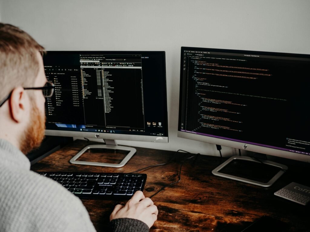 Man working on dual monitors with code on screen, representing Skystta.com’s developer-friendly features