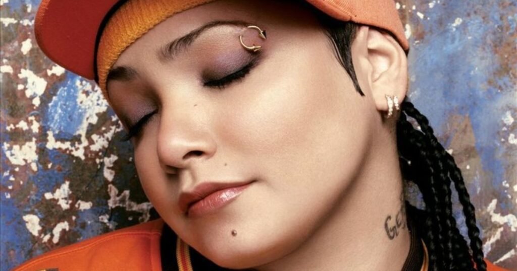 Close-up of a performer with eyes closed, wearing an orange cap and stylish piercings.