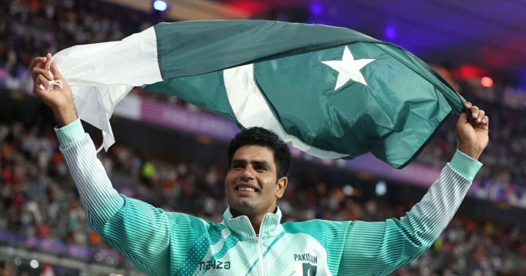Arshad Nadeem smiling while holding the Pakistan flag in his hand, celebrating his achievement.