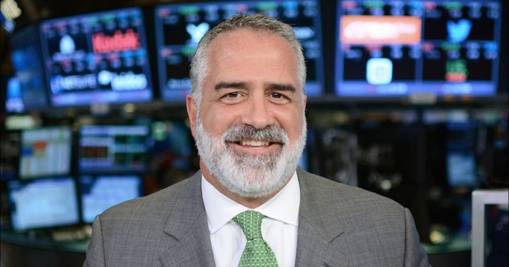 Kenny Polcari smiling in front of stock market screens