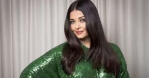 Aishwarya Rai wearing a shimmering green outfit, smiling gracefully in front of a neutral background.