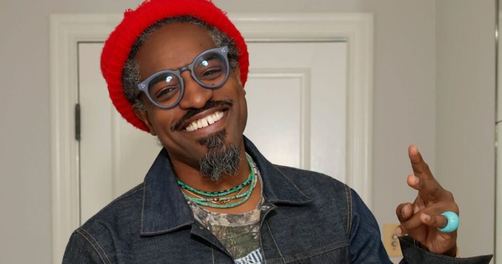André 3000 smiling in a red beanie and denim jacket, showcasing his charismatic presence in film and television.