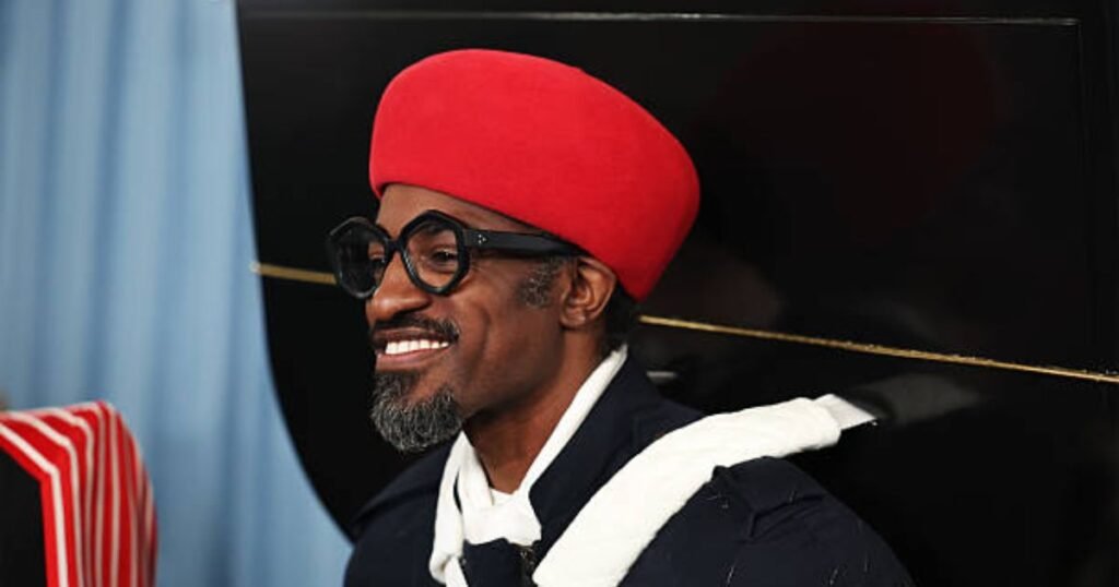 Andre 3000 wearing a red hat and glasses, smiling during a public appearance, representing his music legacy and unique fashion sense.