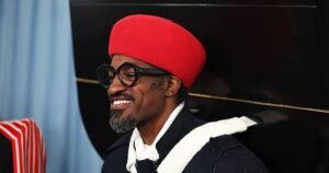 Andre 3000 wearing a red hat and glasses, smiling during a public appearance, representing his music legacy and unique fashion sense.