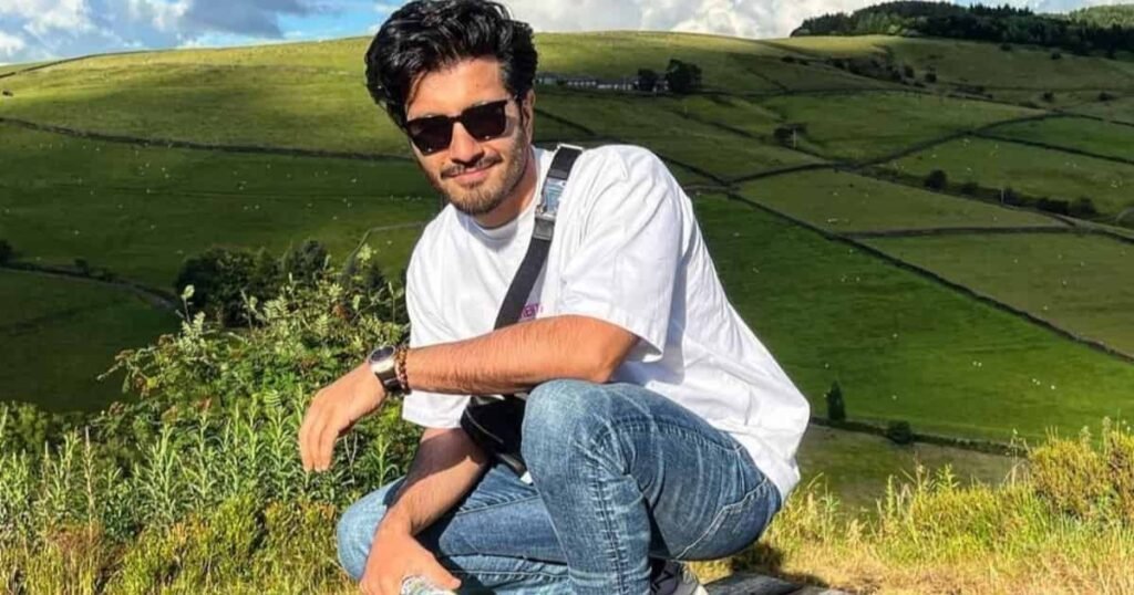 Feroze Khan wearing white t-shirt and sunglasses posing outdoors in green fields