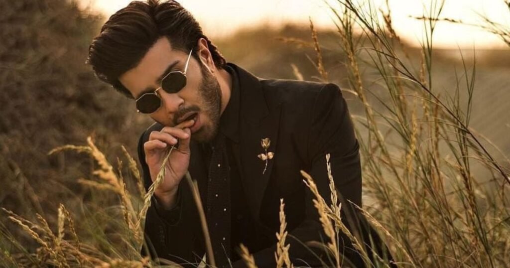 Feroze Khan in black suit and sunglasses sitting in a field