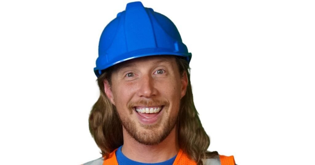 Handyman Hal smiling in a blue construction helmet and orange safety vest, representing his early life roots and educational background that inspired his creative career.