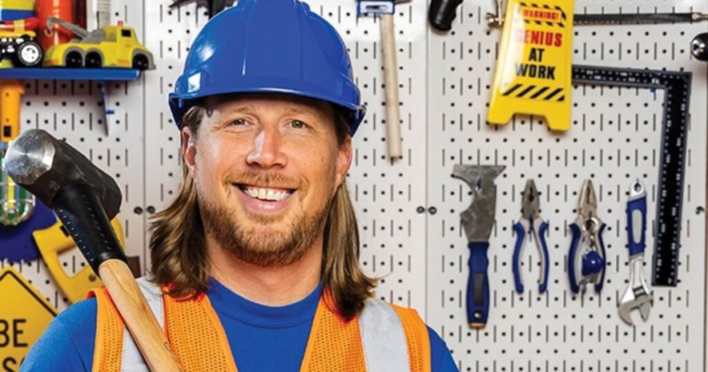 Handyman Hal smiling in a blue hard hat and orange safety vest, holding a hammer in his workshop surrounded by tools, showcasing his professional handyman career.