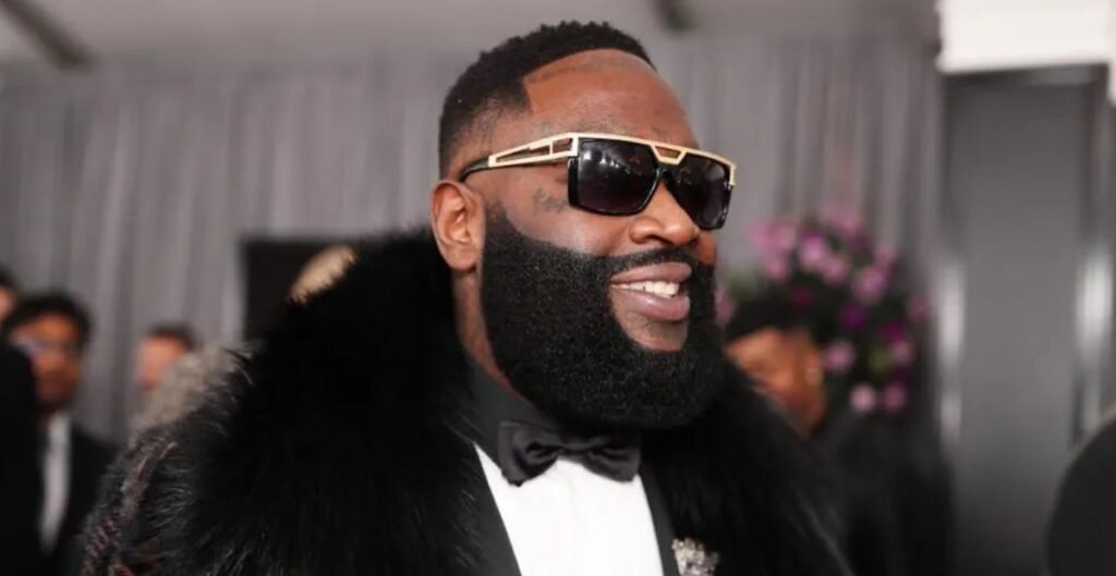 Rick Ross smiling in a tuxedo during a public event representing his successful career development